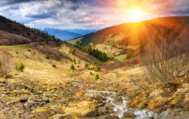Panorama of idyllic landscape in the spring mountains at sunshine. View of the mountain stream flowing among the hills.