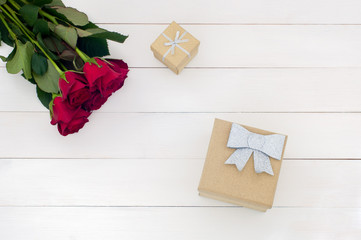 Top flat view of red roses and glitter gift boxes on a white wooden surface (concept)