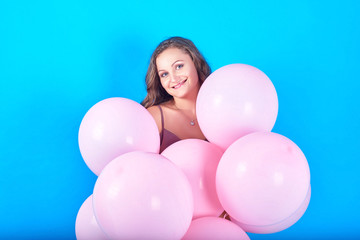 Fototapeta na wymiar Happy smiling young woman having fun with pink helium air balloons over blue background in studio. Girl with curly hair holding pink balloons. Beauty, holidays, birthday, valentine, fashion concept