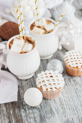 Cups with cacao and marshmallow, cupcakes and different Christmas decorations, wooden background