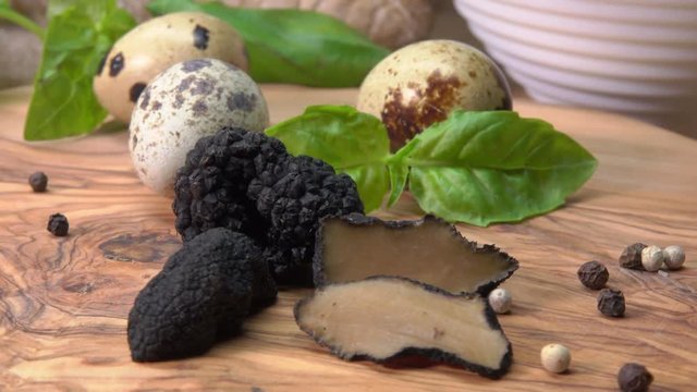 Circular movement of the camera around of black truffles, quail eggs and basil on a wooden board