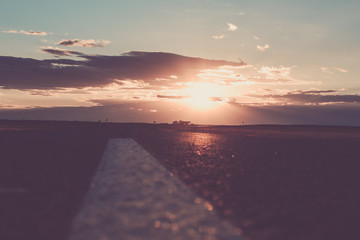 The sunset or the dawn of the sun over a road that goes into the distance. The rays of the sun, making their way through the clouds above the road.