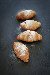 four croissants with a fruit filling, sprinkled with powdered sugar on a dark gray background