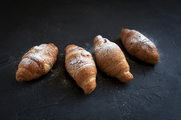 four croissants with a fruit filling, sprinkled with powdered sugar on a dark gray background
