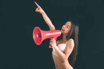 young woman shouting with an megaphone. Young woman with long black hair stands isolated on black...