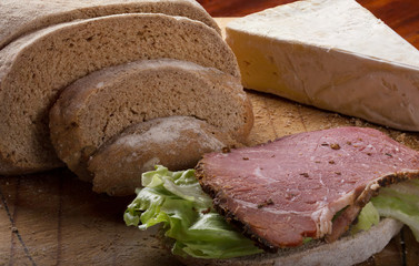 Pastrami and lettuce on a slice of Rye bread with brie cheese and rye bread with slices of rye bread in background