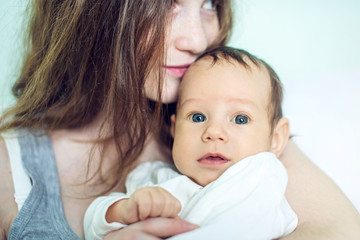 Happy caring mother holding baby boy in the bedroom. Concept of the tenderness of motherhood and family values