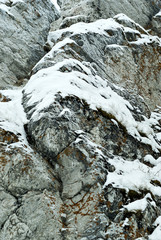 vertical background: a fragment of the wall of a natural cliff with snow-covered ledges..
