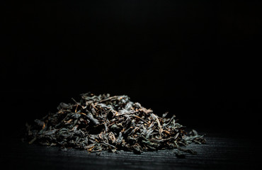 Heap of black tea leaves on the old dark wooden background with copy space