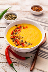 Pumpkin soup with cream and seasoning in white bowl on rustic wooden background