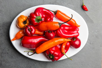 Chili and bell pepper on white plate, slate background, top view