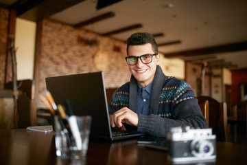 Authentic portrait of young smiling businessman looking at camera with laptop in office. Hipster...