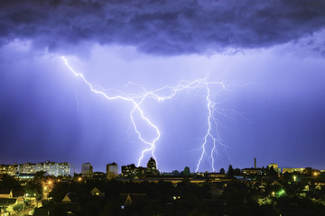 Lightning over the city in the night sky strikes the roof of the house