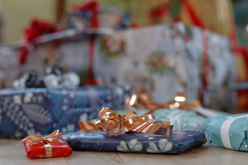 Pile of Christmas presents wrapped in colorful gift paper decorated with golden ribbon. Short depth of focus
