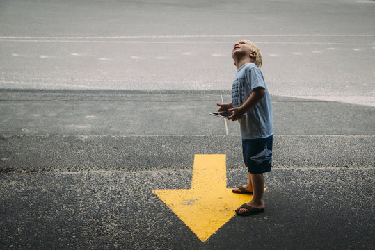 Side view of boy with tablet computer looking up while standing by arrow symbol on road
