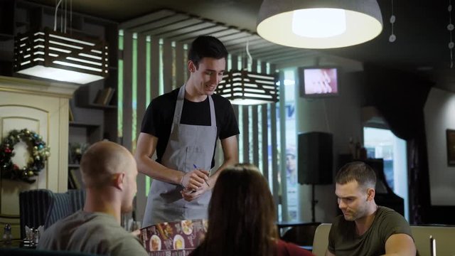 the waiter takes an order from a group of people who chose food from the menu, they will soon receive their order