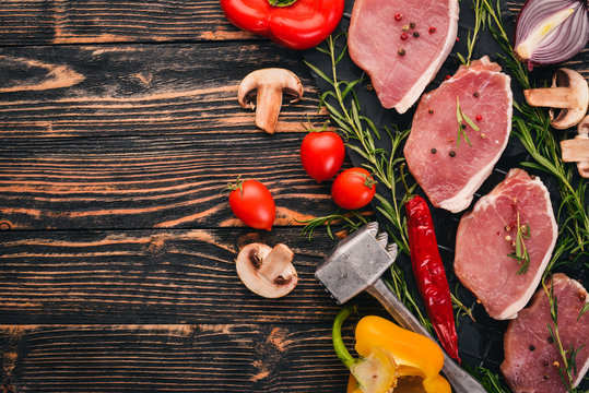 Beef steak with fresh vegetables and rosemary and spices on a black wooden background. Top view. Free space for text.