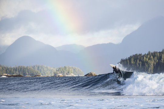 Rear view of man surfboarding on waves in sea against rainbow