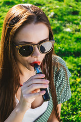 Happy fashion smiling Woman in sunglasses smoking vape on street,smoke