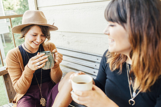 Smiling female friends having coffee while sitting on wooden bench