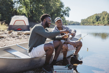 Friends adjusting fishing tackles on boat at lakeshore