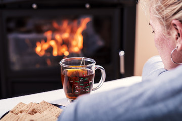 The woman in front of the fireplace reads the book and drinks tea