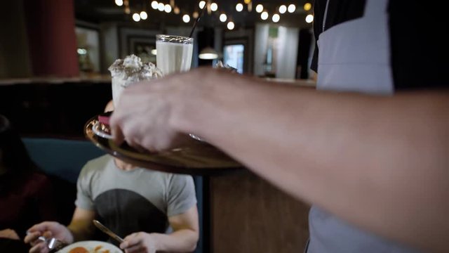 A close shot at the waiter's hand, who carries a tray of drinks, an employee of the restaurant brought milk shakes