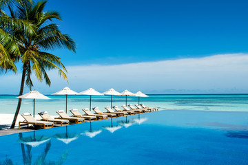 Large infinity pool on the shores of the Indian Ocean with sunbeds and umbrellas in the shade of...