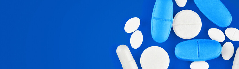 Assorted pharmaceutical medicine pills, tablets and capsules on blue background. The cure for coronavirus.
