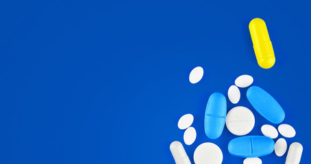 Assorted pharmaceutical medicine pills, tablets and capsules on blue background