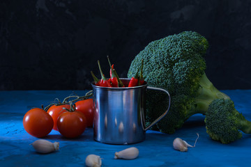 Beautiful still life in a low key. Broccoli, garlic and tomatoes. Chili pepper in a bucket. Unusual...