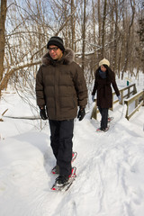 Fototapeta na wymiar Ethnic couple snowshoeing in the forest near a waterfall