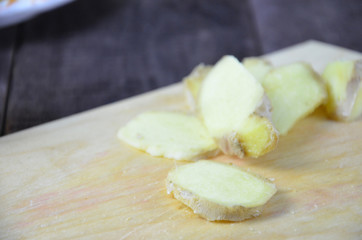 Ginger on cutting board, jar of honey, dried lemon slice, cinnamon and grater on kitchen table. Selective focus.