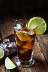 Rum and cola Cuba Libre drink with brown rum, cola, ice and lime on rustic wooden table