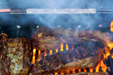 Grilled pork ribs on the flaming grill cooking on barbecue grill for