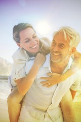 Obraz premium Man giving his smiling wife a piggy back at the beach