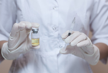 The medical cosmetologist holds a syringe for injection and ampoule with medicine in the beauty...