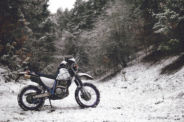 Fototapeta premium Motocykl w zimowym lesie śnieg na tle ośnieżonych drzew. Zimowa ekstremalna zabawa. Motocykle zimą. ekstremalna zabawa zimą na motocyklu, podróż enduro off road dual sport