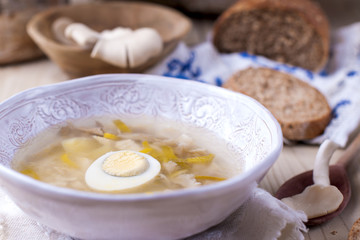 white plate with soup with mushrooms and egg. Wooden background, bread and a spoon