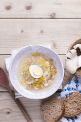 white plate with soup with mushrooms and egg. Wooden background, bread and spices