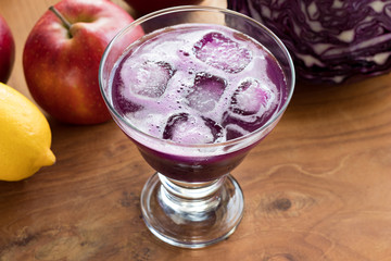 Purple cabbage juice with ice cubes in a glass on a wooden table
