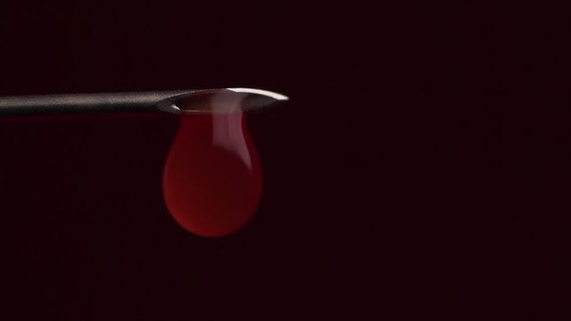 Drops of blood leaking from the needle of a syringe piston. Drop of blood falling from syringe on black background, Macro shot