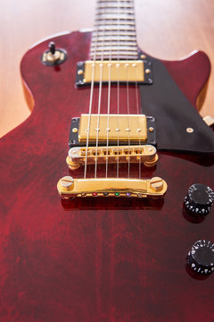 Shiny Wine Red Guitar With Golden Hardware on A Wooden Table With Focus on the Stop Bar