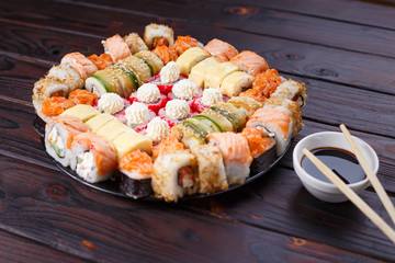 Tasty appetizing multicolored sushi rolls set, served with soy sauce and chopsticks on wooden table