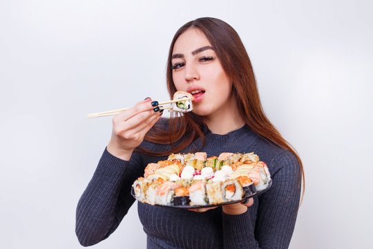 Young beautiful woman enjoy eating sushi, studio shoot on white background with copy space. Japanese food