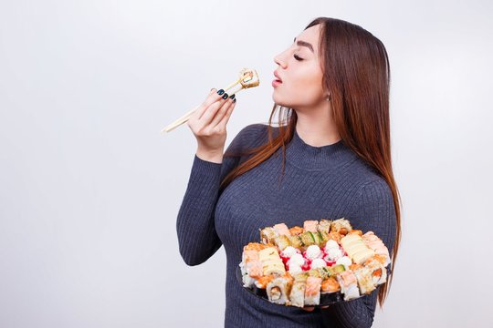 Portrait of young attractive woman eating sushi, studio shoot on white background with copy space. Japanese food, restaurant concept
