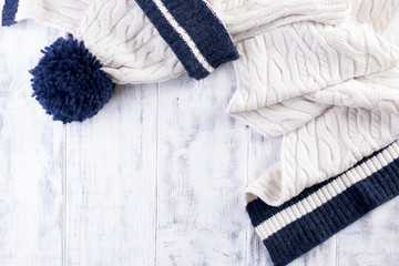 knitted winter scarf and a white cap with a blue strip on a white wooden background. Copy Space for Text Happy New Year Greeting Card Winter Theme