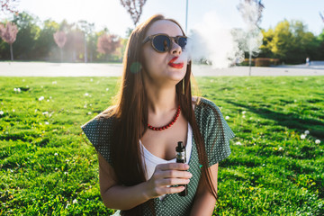 Happy fashion smiling Woman in sunglasses smoking vape on street,smoke