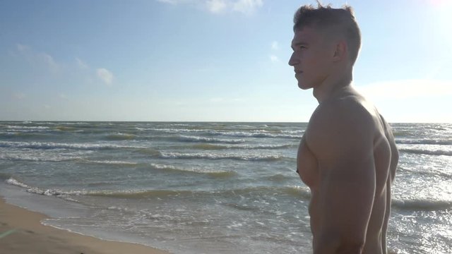 Handsome wet muscular man walking on beach