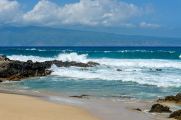 Fototapeta na wymiar Island Beach - Strong blue waves running onto a rocky island beach, with another tropical island in the background. Maui, Hawaii, USA.